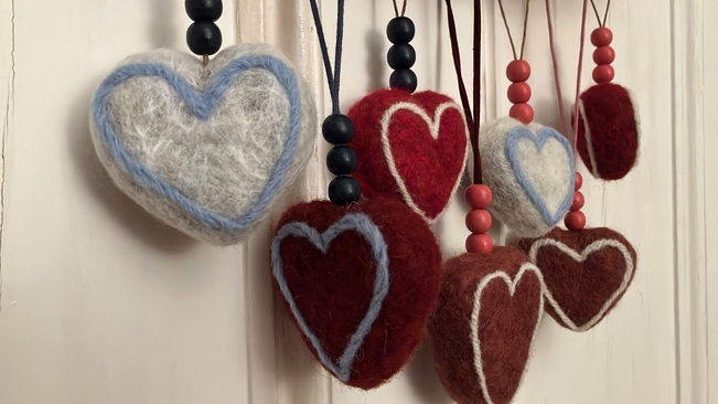 A cute collection of seven needle-felted heart decorations, hanging against a wall