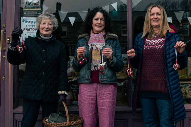 Three crafters stood in front of a shop, proudly displaying their creations